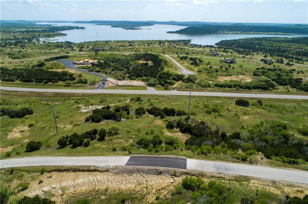 An aerial view of a road leading to a lake surrounded by trees and grass.