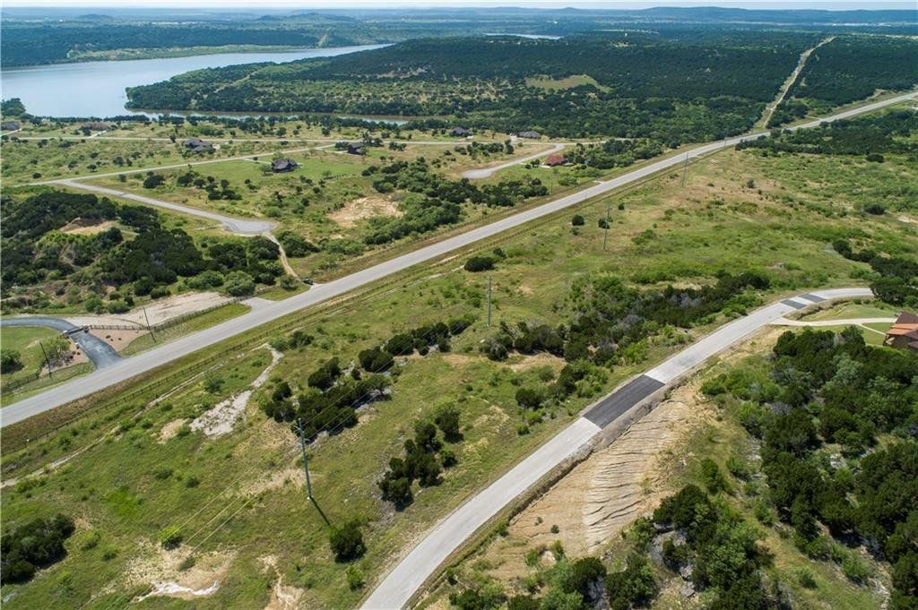 An aerial view of a road going through a lush green field next to a lake.