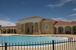 A large house with a pool in front of it behind a fence.