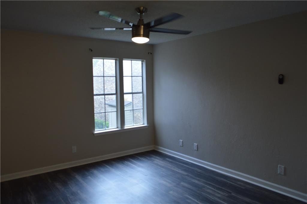 An empty room with a ceiling fan and two windows.