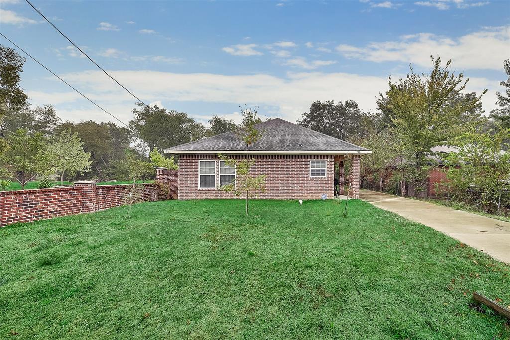 A brick house is sitting on top of a lush green lawn next to a dirt road.