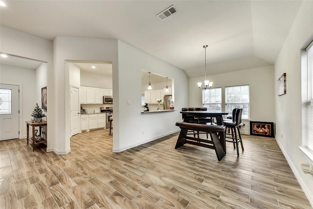 A living room with a wooden table and chairs and a kitchen in the background.