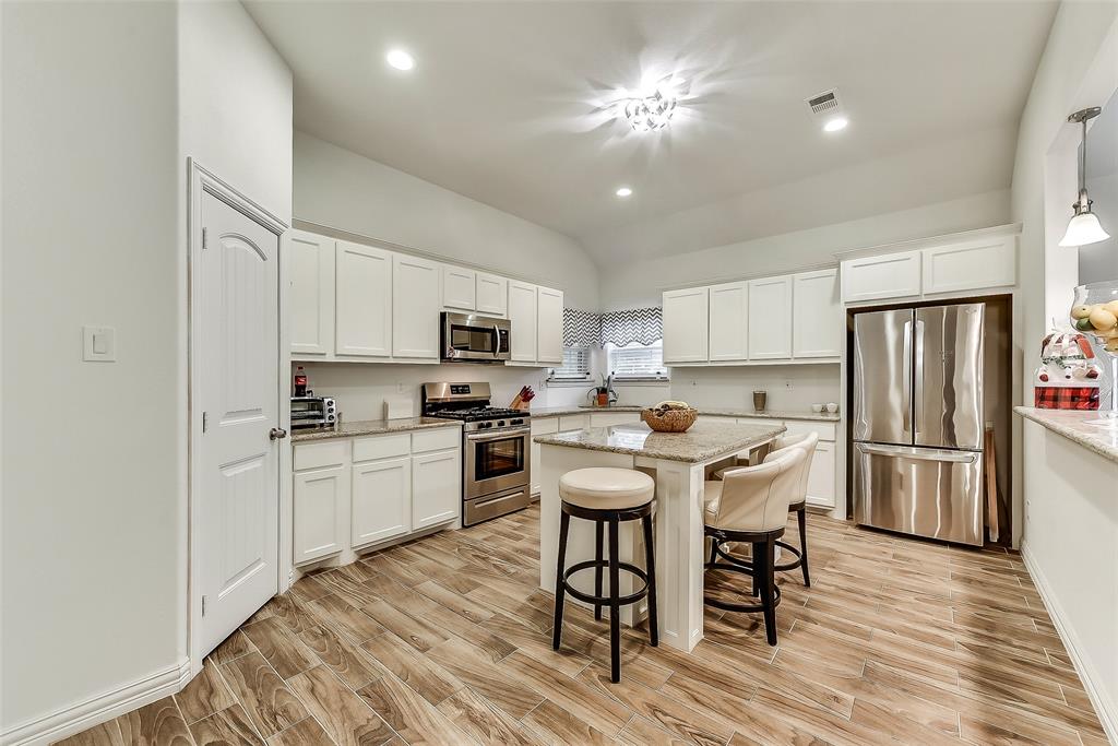 A kitchen with white cabinets , stainless steel appliances , and a large island.