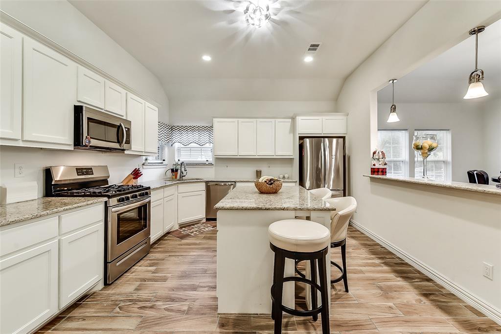 A kitchen with white cabinets , stainless steel appliances , and a large island.