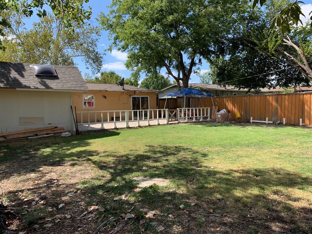 The backyard of a house with a large lawn and a wooden fence.