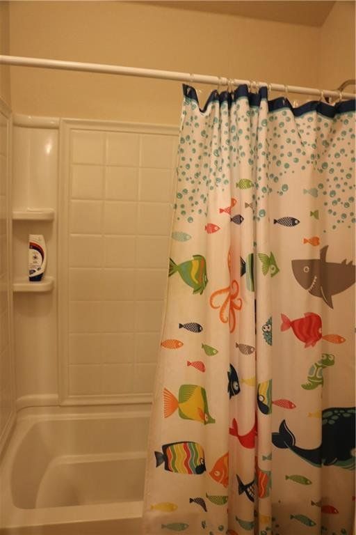 A bathtub with a shower curtain with fish on it