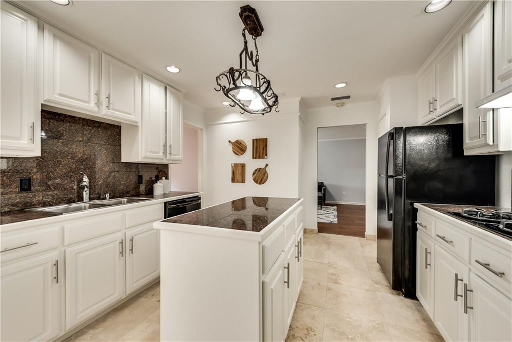 A kitchen with white cabinets , black appliances and a large island.