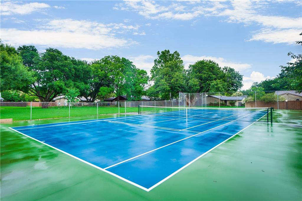 A blue and green tennis court with trees in the background.
