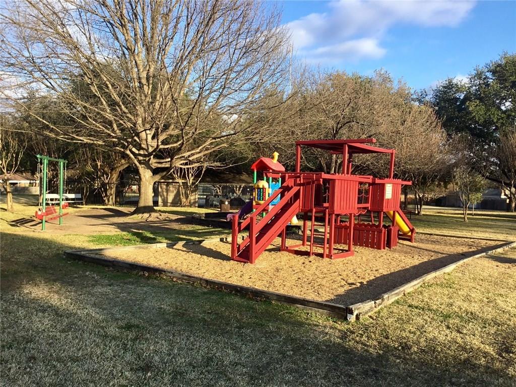A red playground set in a park with trees in the background.