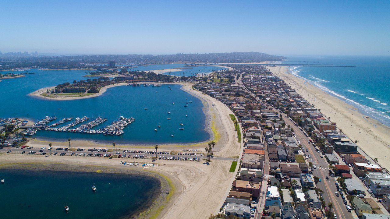an aerial view of a beach with a harbor and a city in the background .