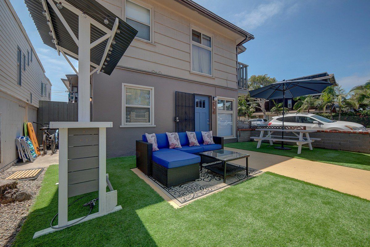 a backyard with a couch , table and umbrellas in front of a house .