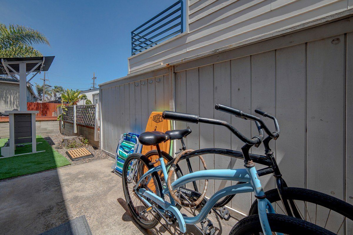 two bicycles are parked on the side of a building next to a surfboard .