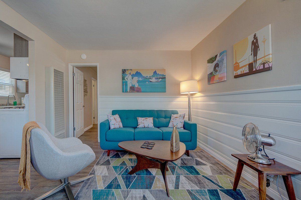 a living room with a blue couch , coffee table , chair and paintings on the wall .