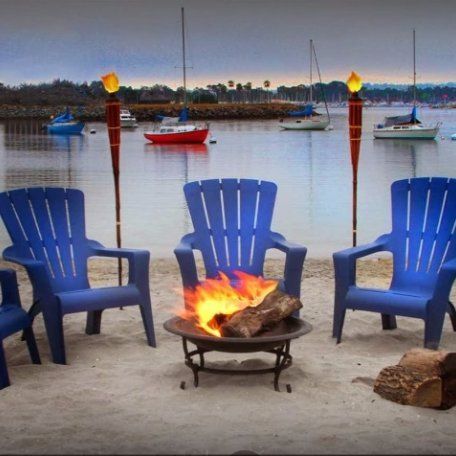 Three blue chairs sit around a fire pit on the beach