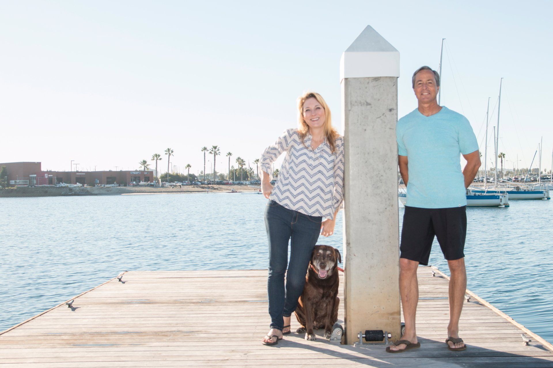 a man and a woman are standing on a dock with a dog .