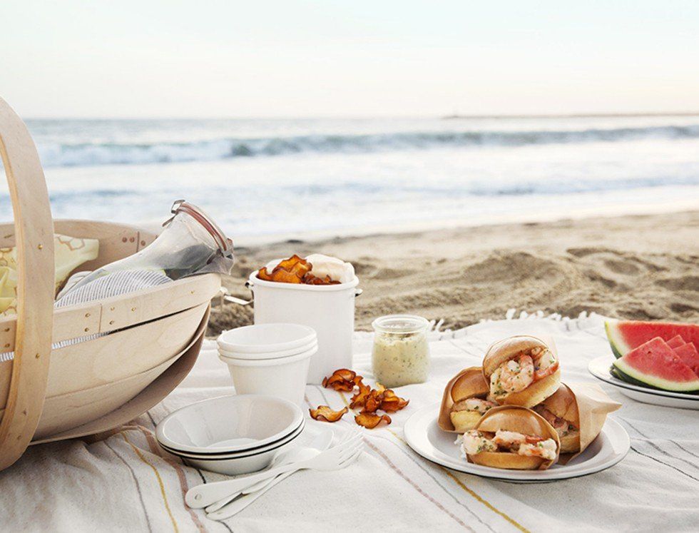 a picnic on the beach with a basket of food and watermelon .