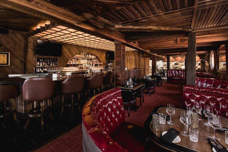 a restaurant with a bar , tables , chairs and a red chair .