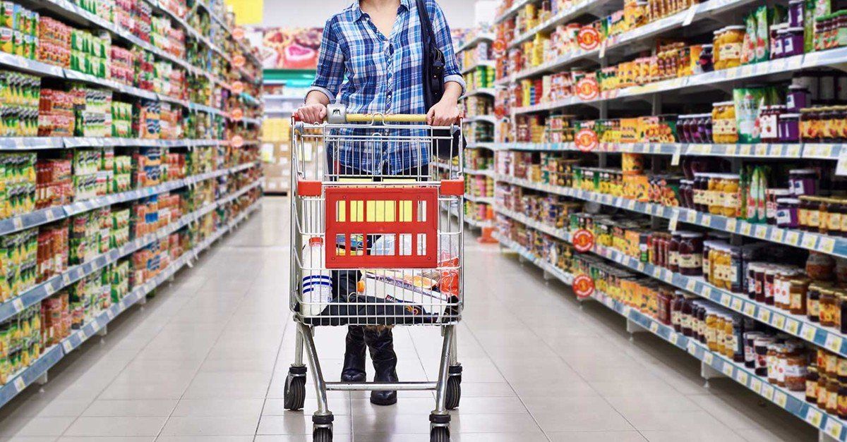 A woman is pushing a shopping cart down an aisle in a supermarket.