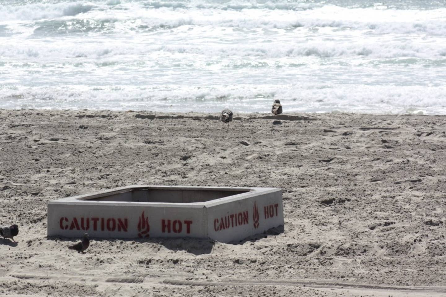 A fire pit on a beach that says caution hot