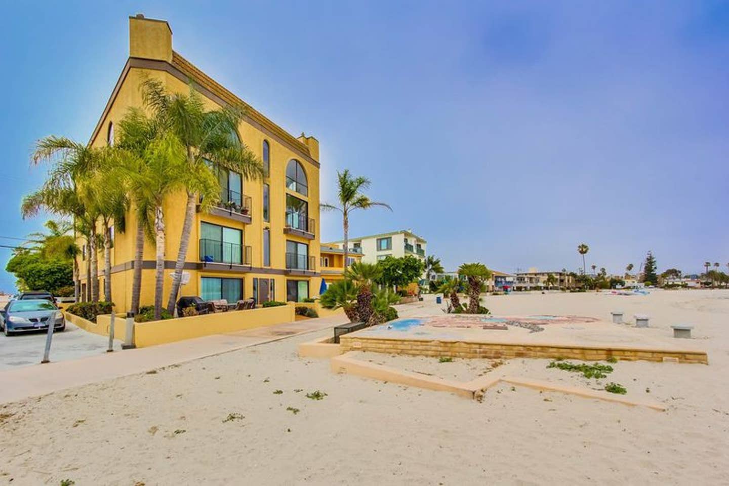 A large yellow building is sitting on top of a sandy beach.