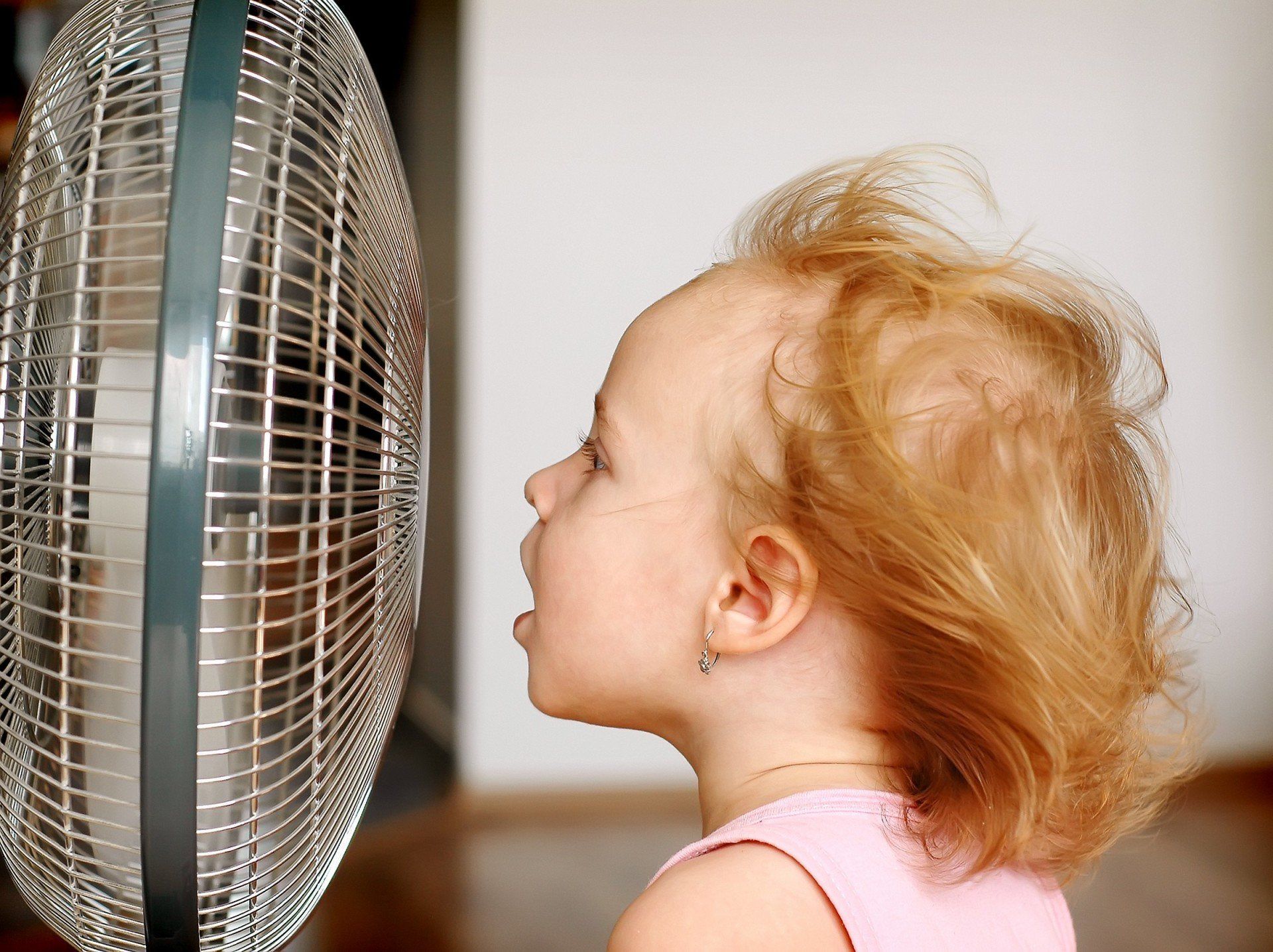 a little girl is standing in front of a fan .