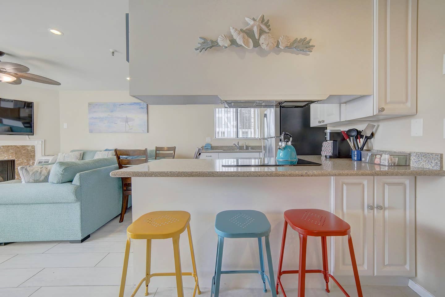 A kitchen with three colorful stools and a blue couch.