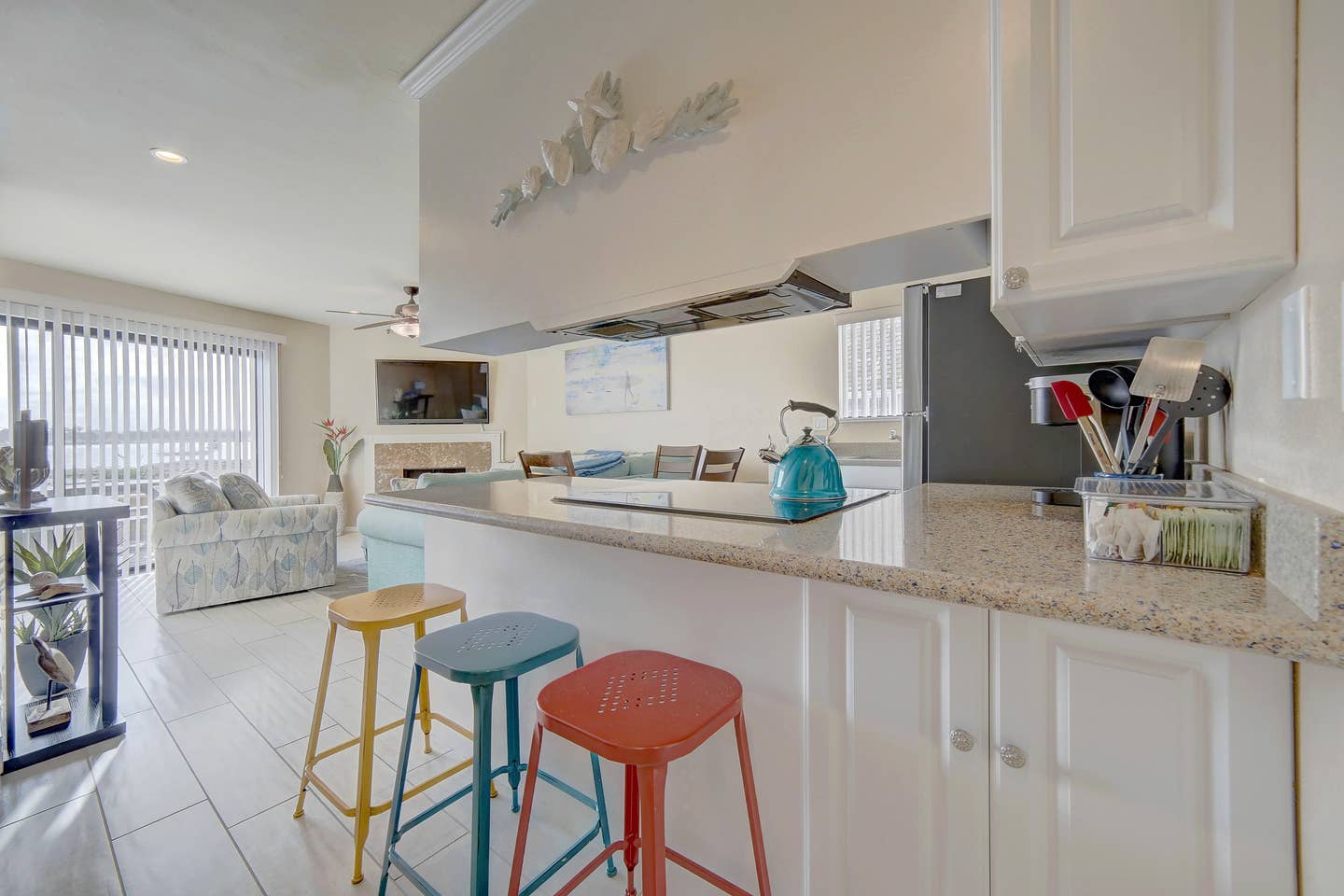 A kitchen with white cabinets , granite counter tops , and colorful bar stools.