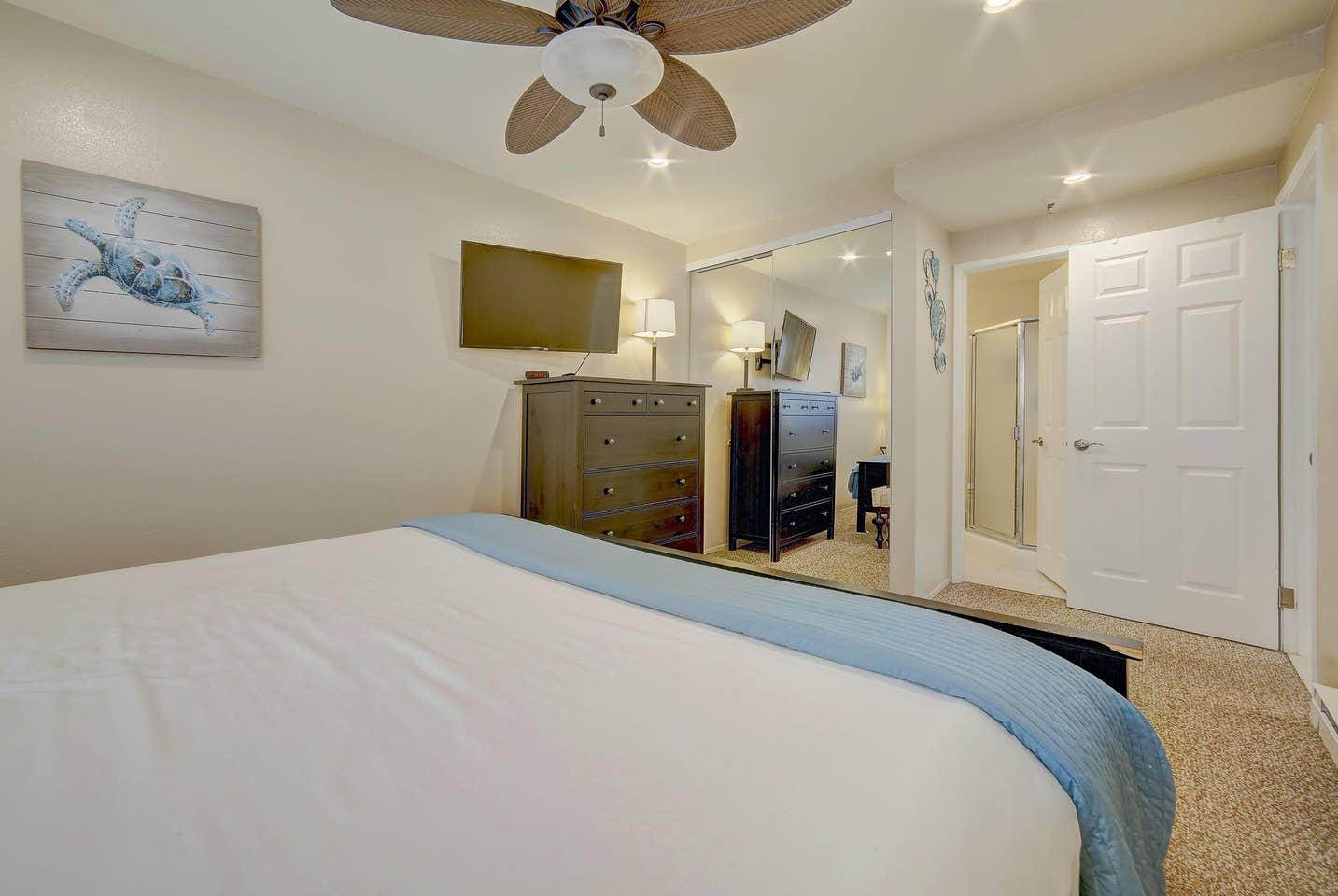 A bedroom with a bed , dresser , television and ceiling fan.