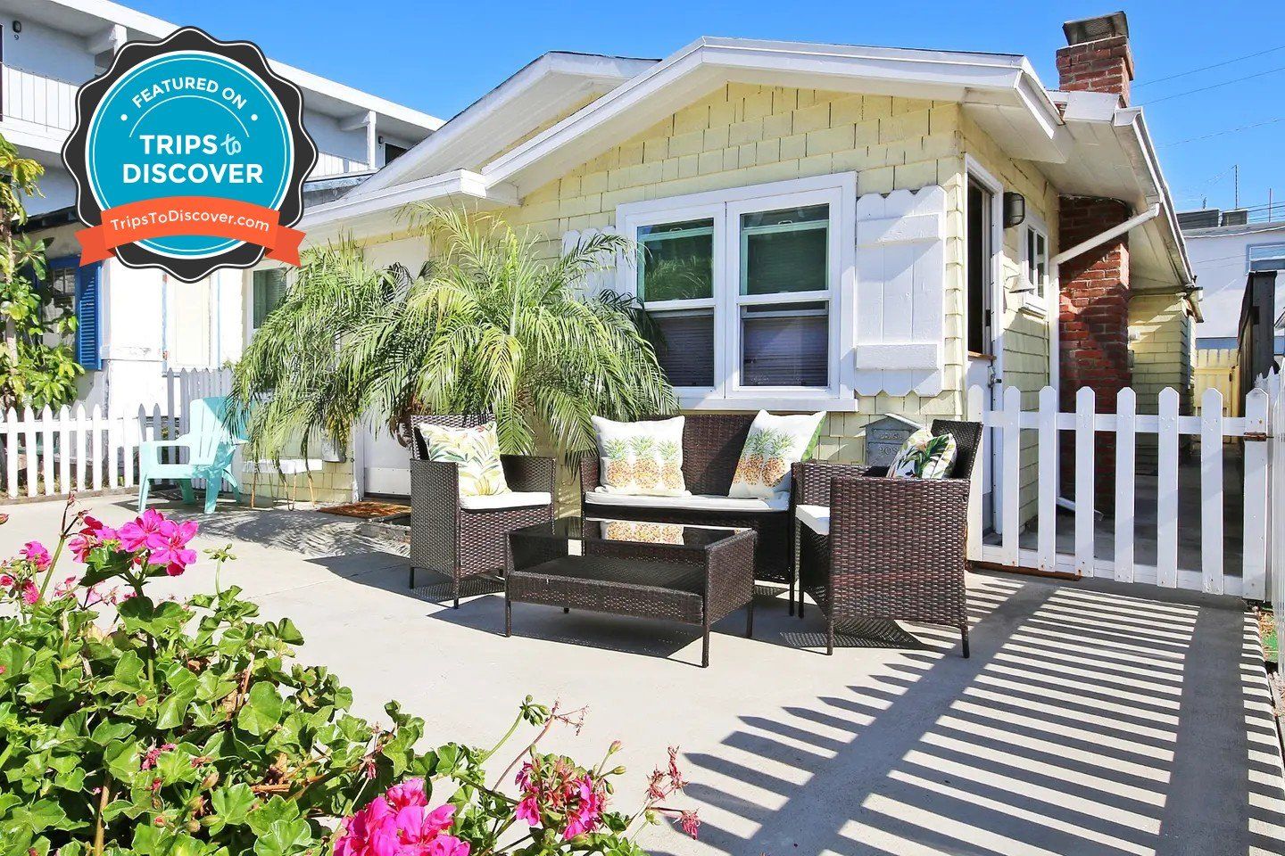 a yellow house with a white picket fence and patio furniture