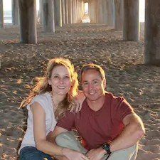 a man and a woman are sitting under a bridge on the beach .