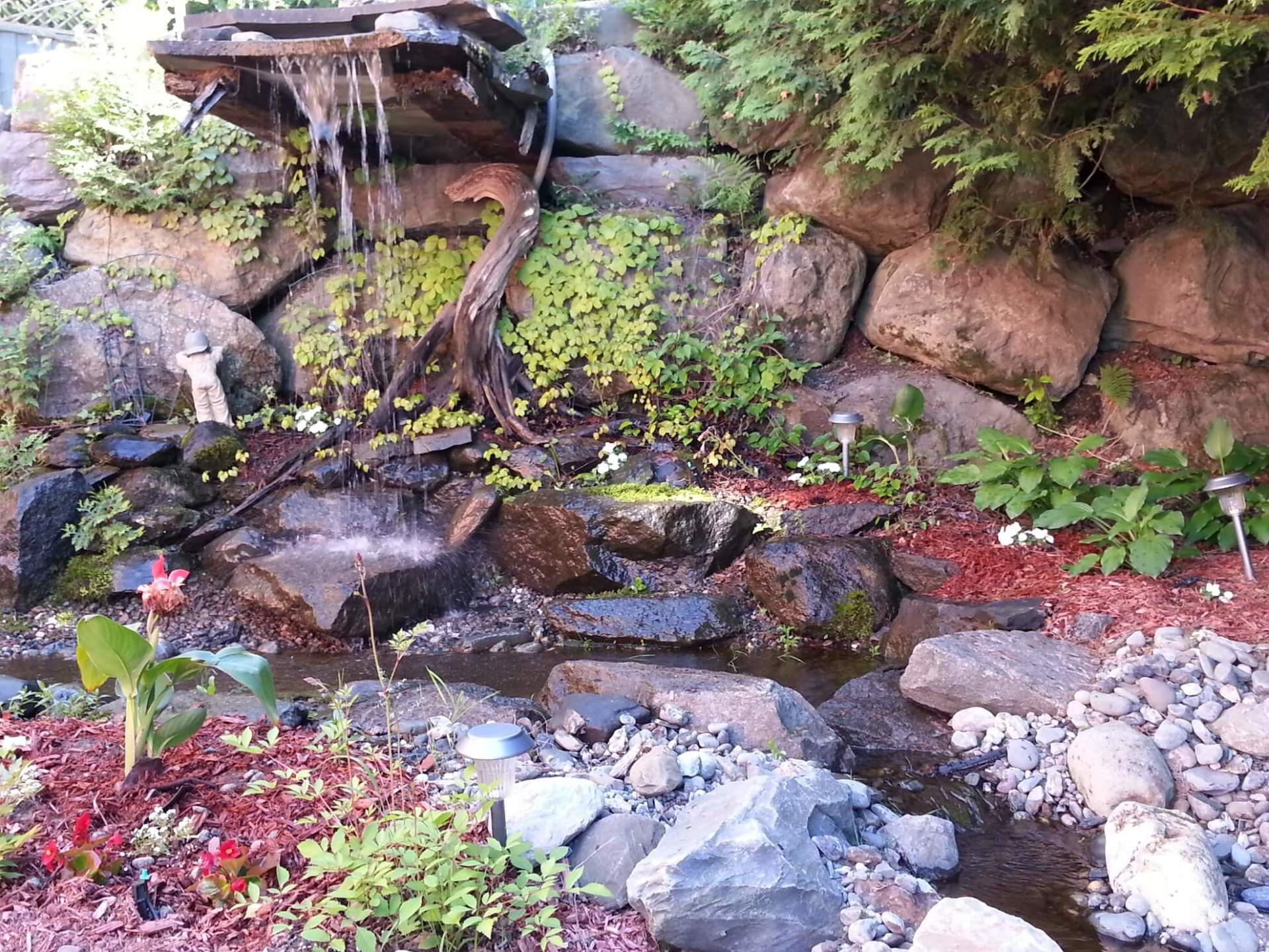 Une cascade est entourée de rochers et de plantes dans un jardin.
