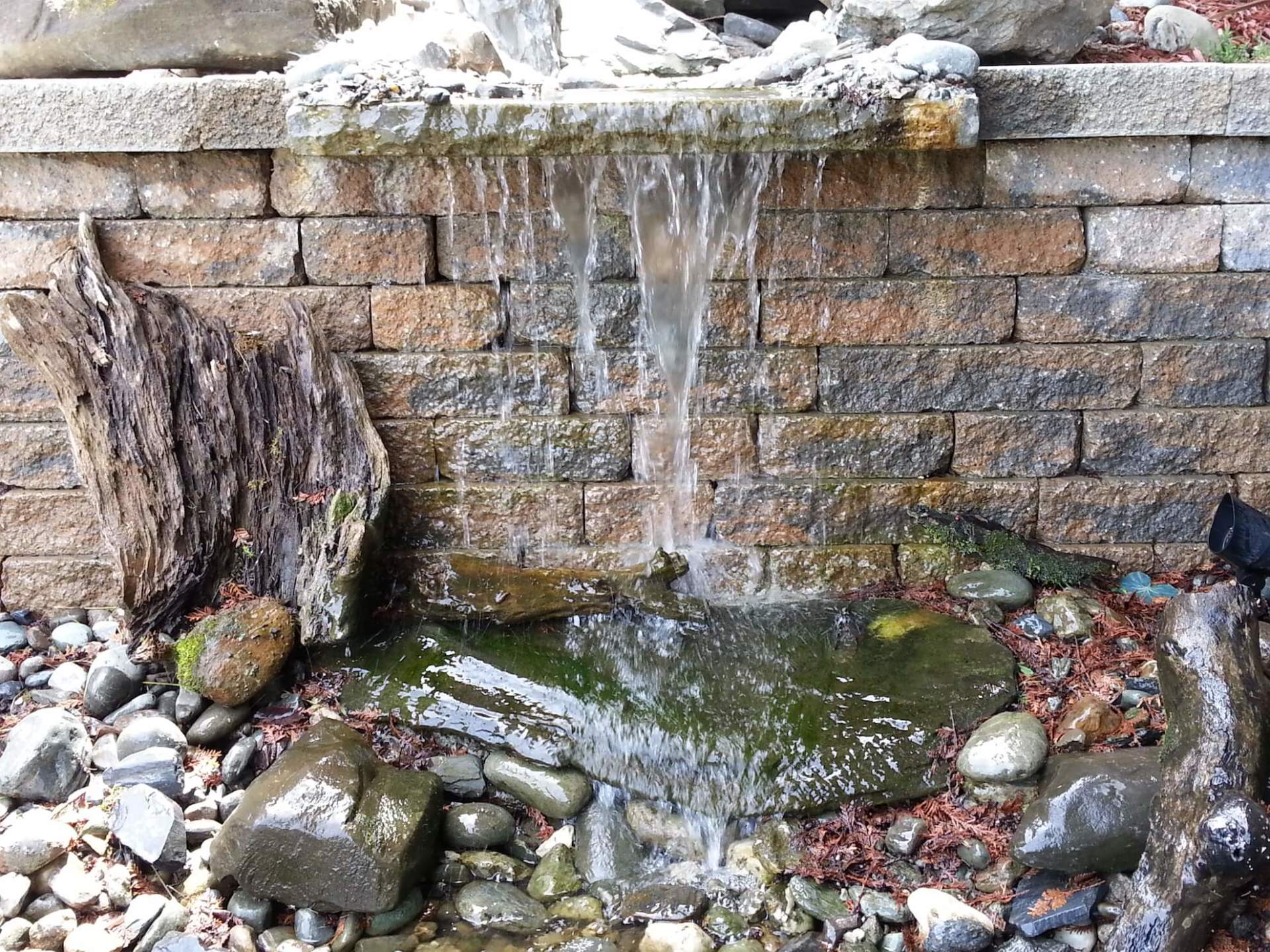 Une petite cascade est entourée de rochers et d'un mur de briques.