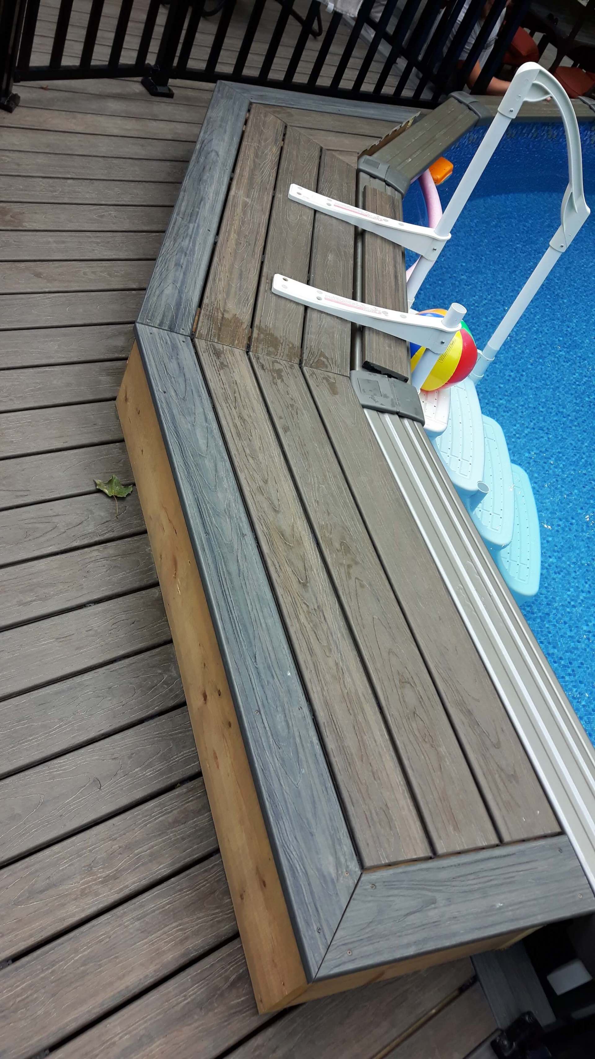 Une terrasse en bois à côté d'une piscine avec un ballon de plage dans l'eau.