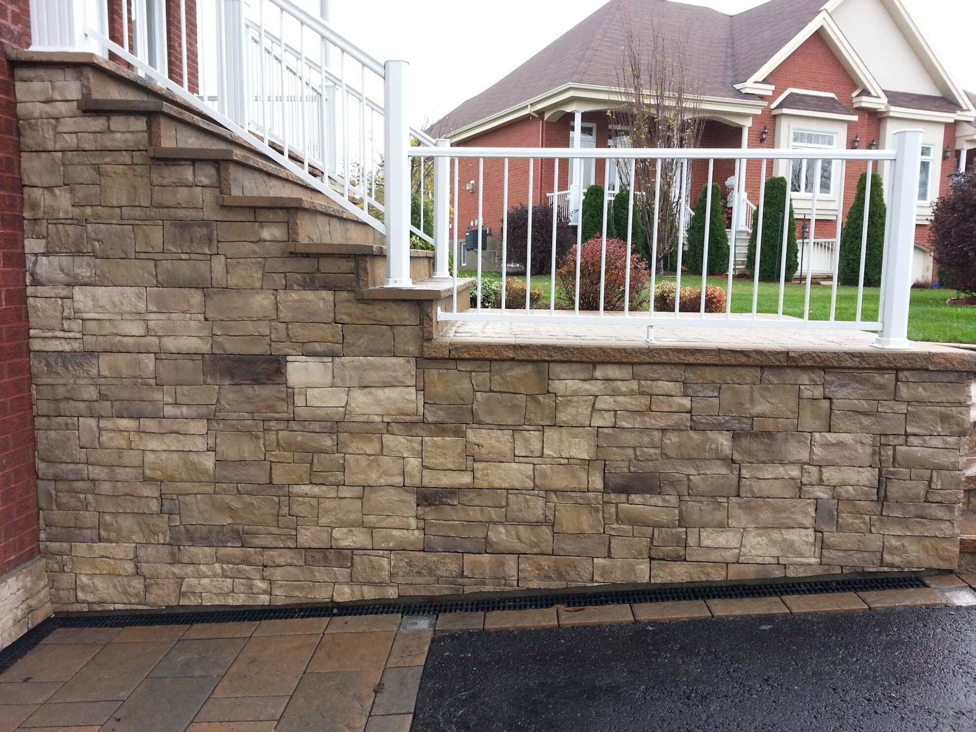 Un mur de pierre avec des escaliers et une balustrade blanche devant une maison