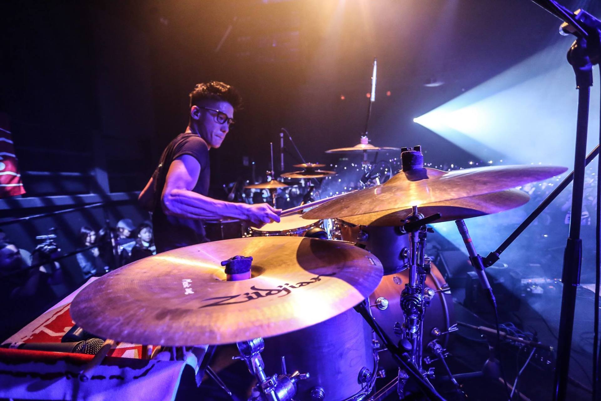 A man is playing drums on a stage in a dark room.
