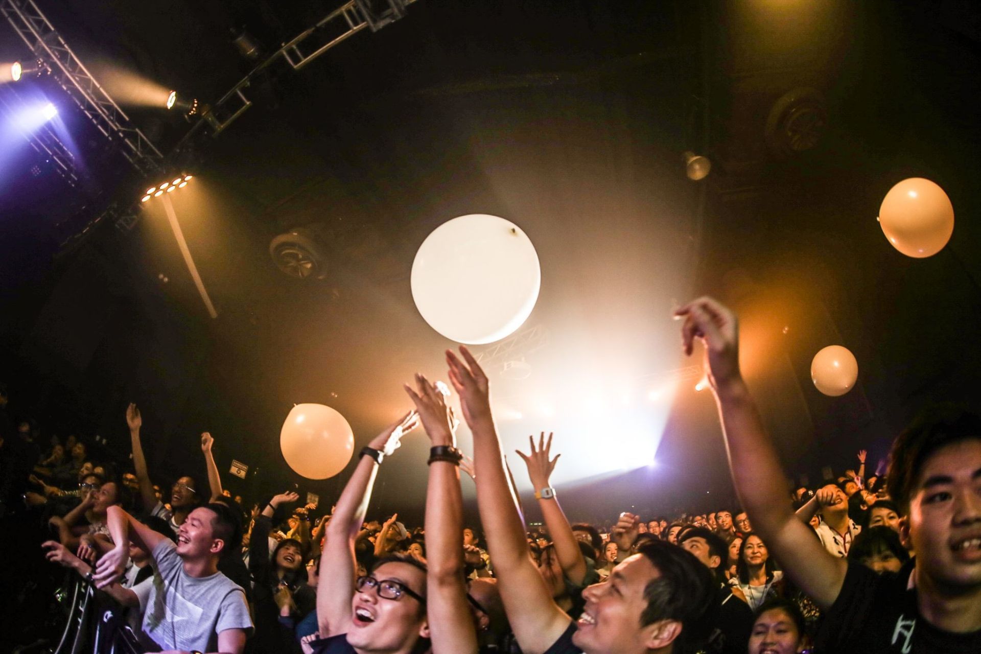 A crowd of people are holding balloons in the air at a concert.