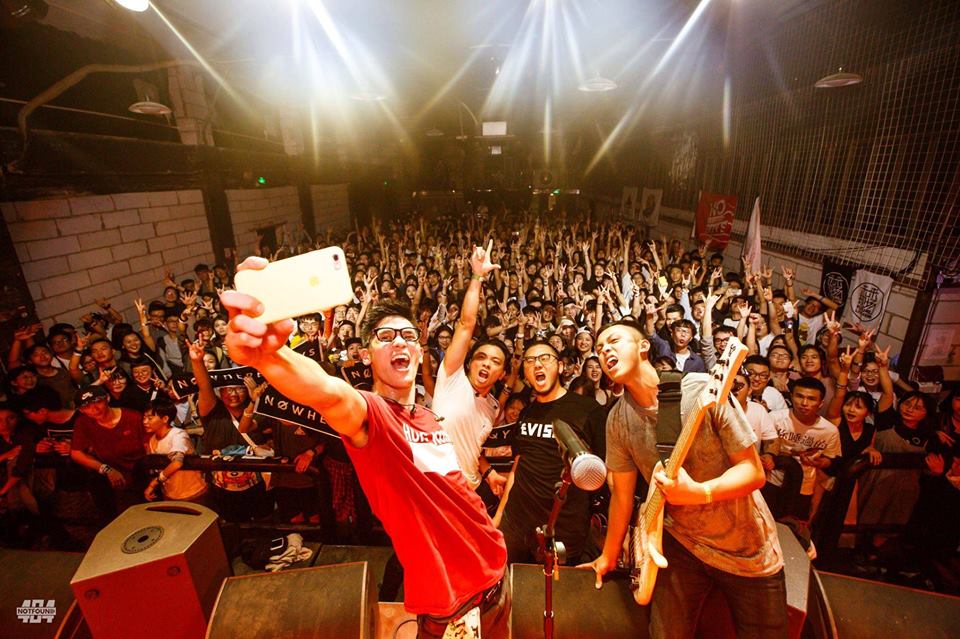 A group of people are standing on a stage taking a selfie in front of a crowd.