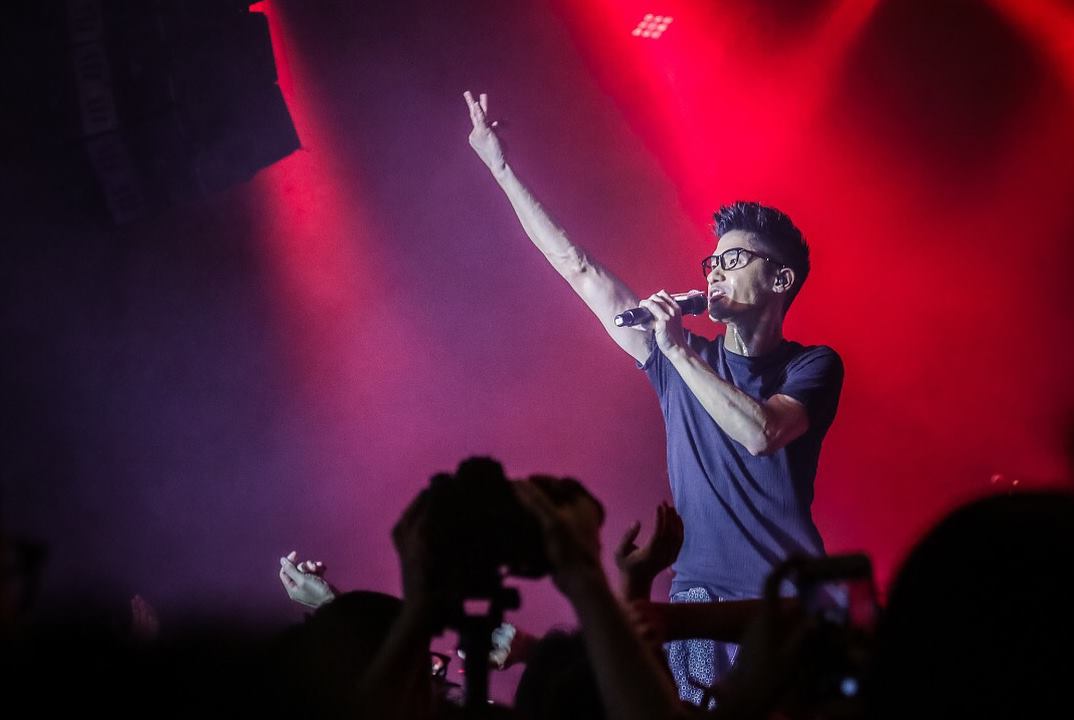 A man is singing into a microphone on a stage in front of a crowd.
