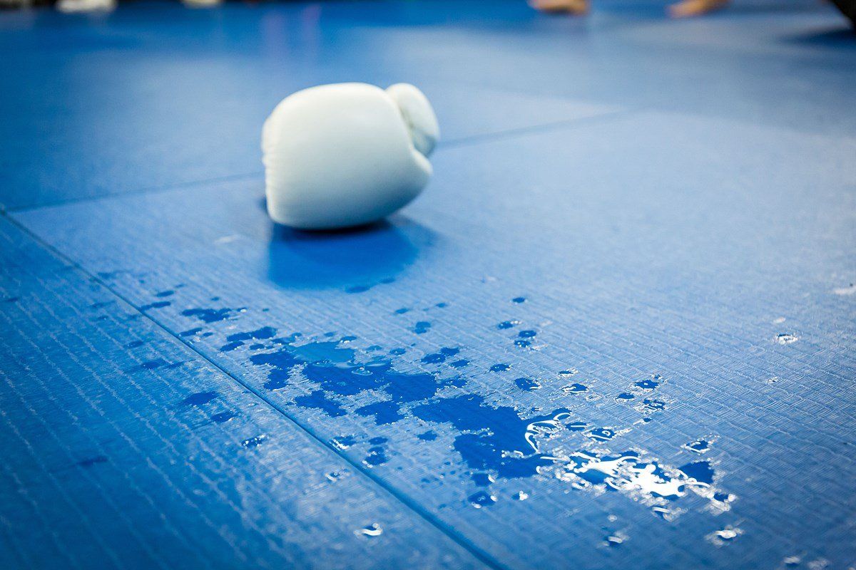 A white boxing glove is laying on a blue mat.