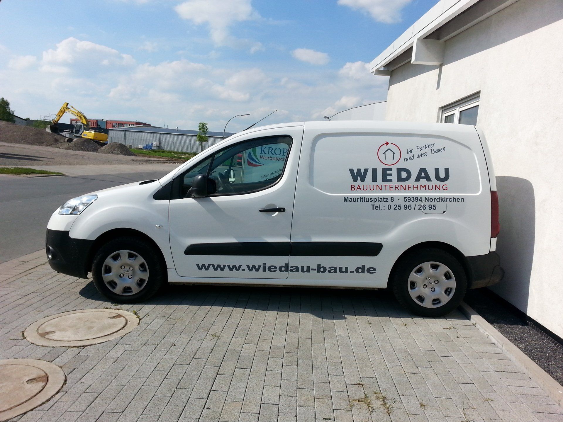 A white wiedau van is parked in front of a building