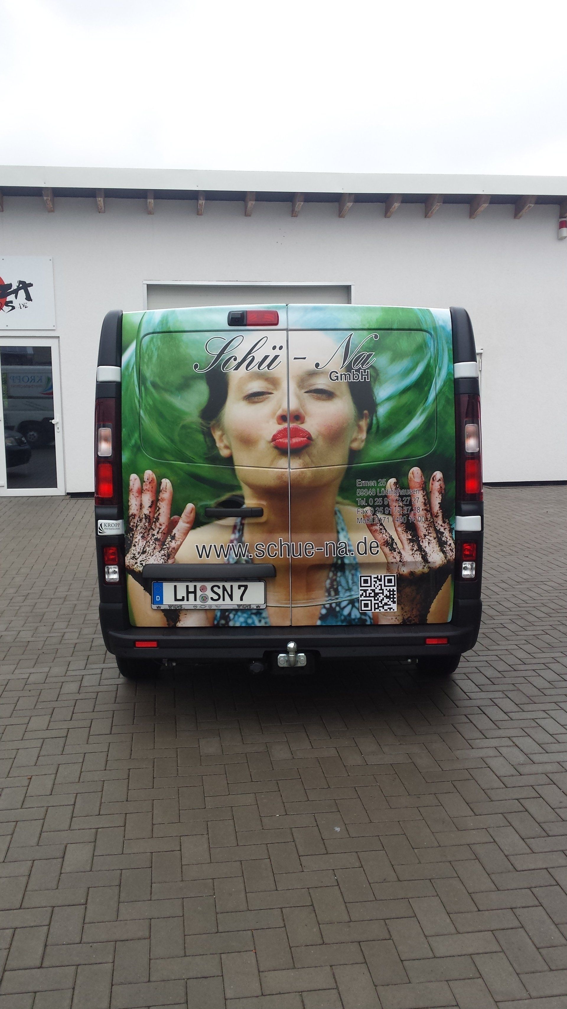 A van with a picture of a woman on the back is parked on a brick driveway.