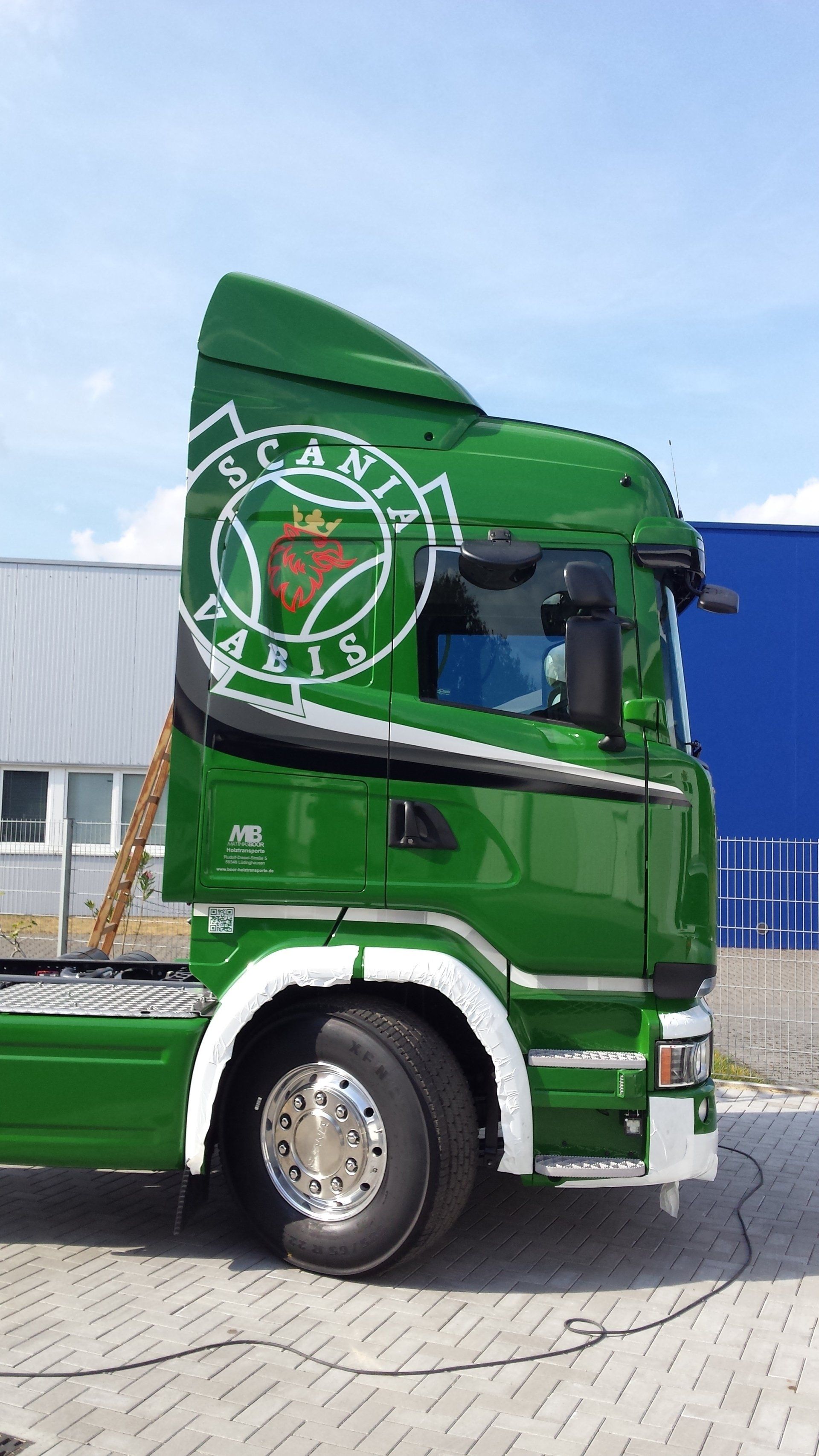 A green semi truck is parked in front of a blue building.