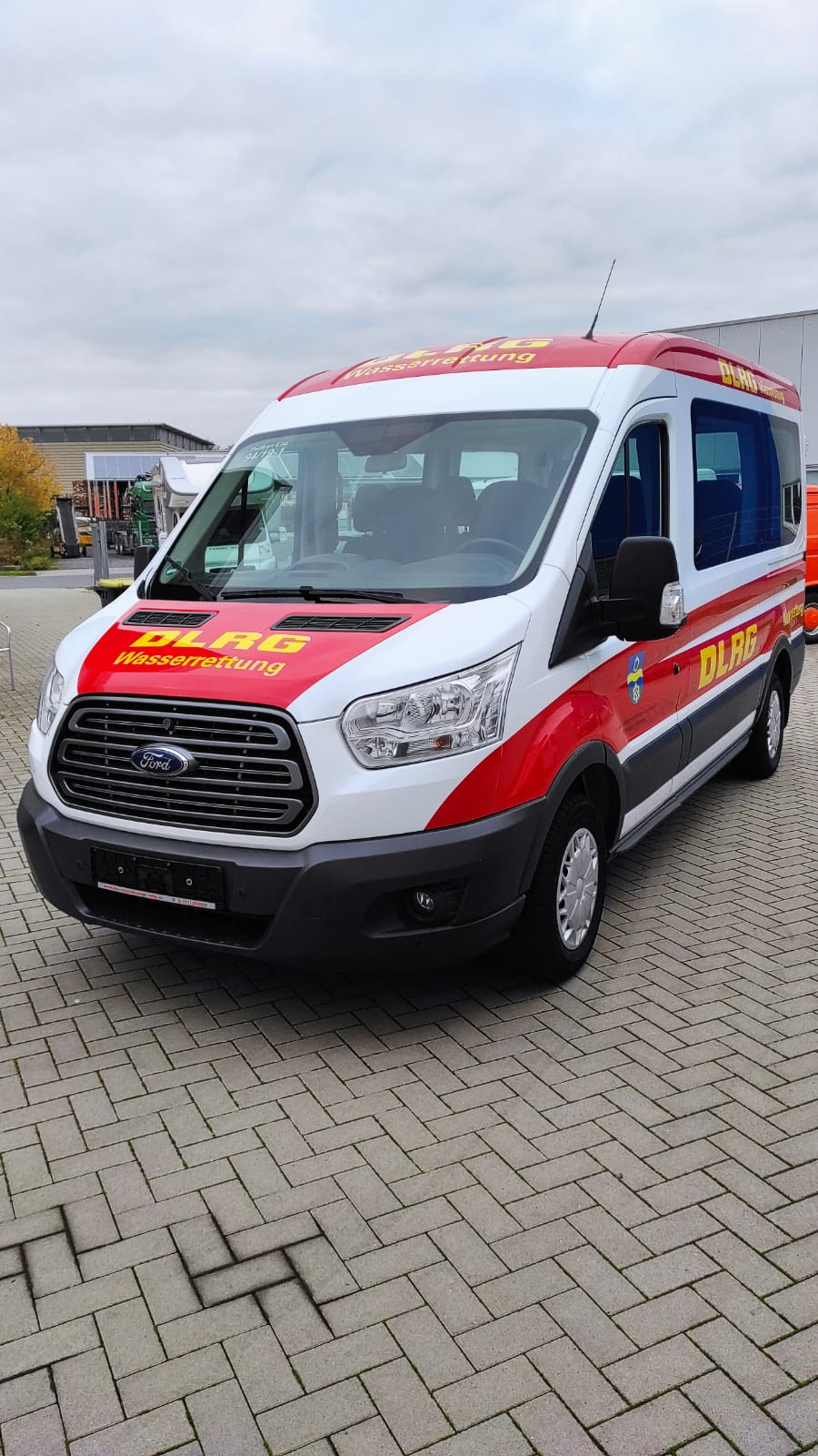 A red and white van is parked on a brick driveway.