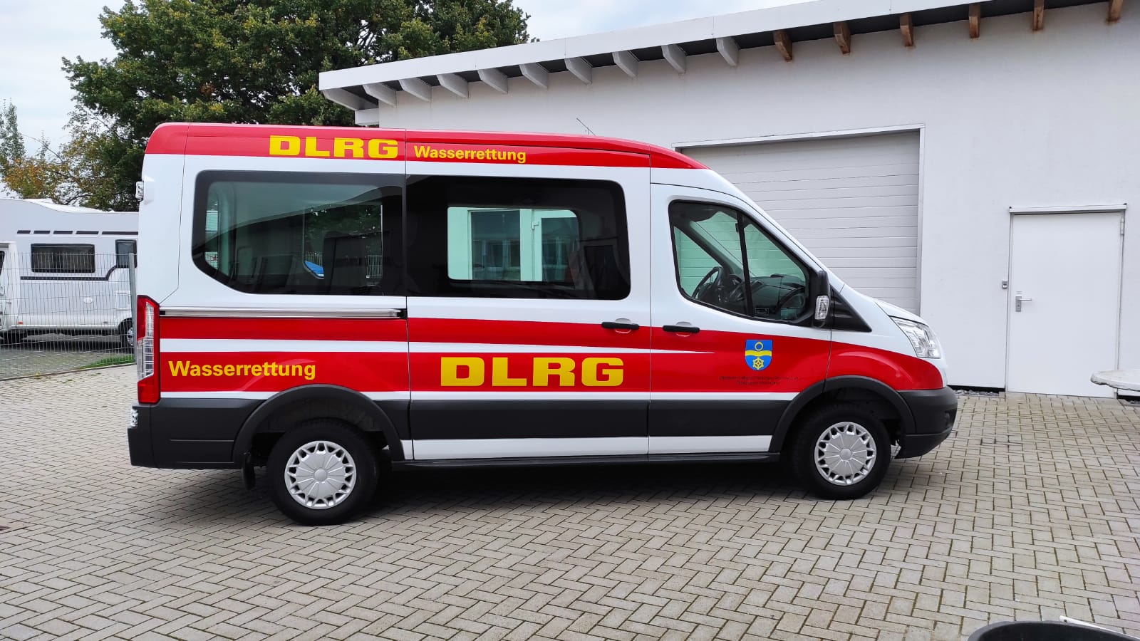 A red and white van with the word dlrg on the side is parked in front of a garage.
