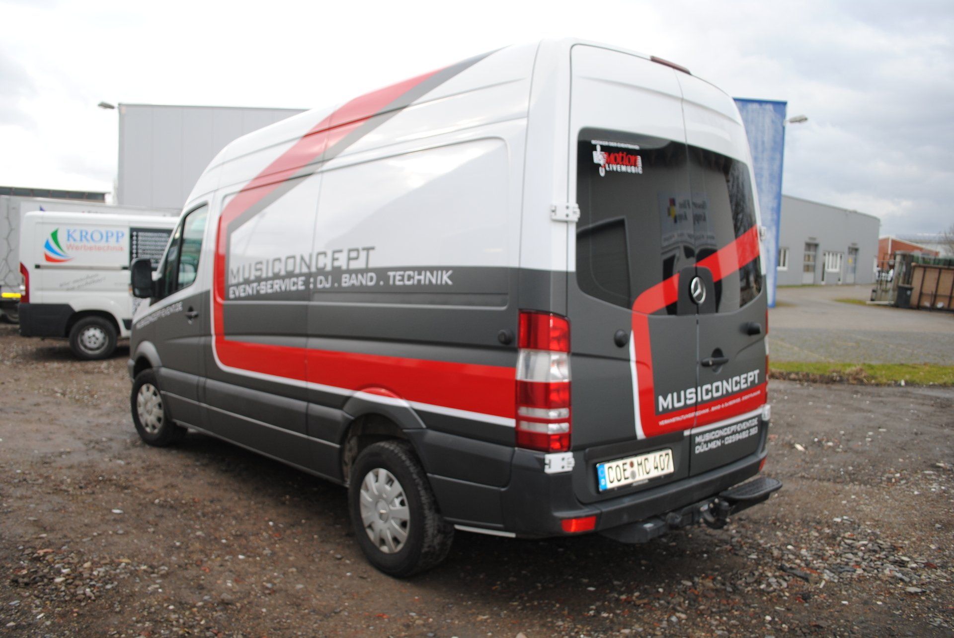 A red and white van is parked in a gravel lot.