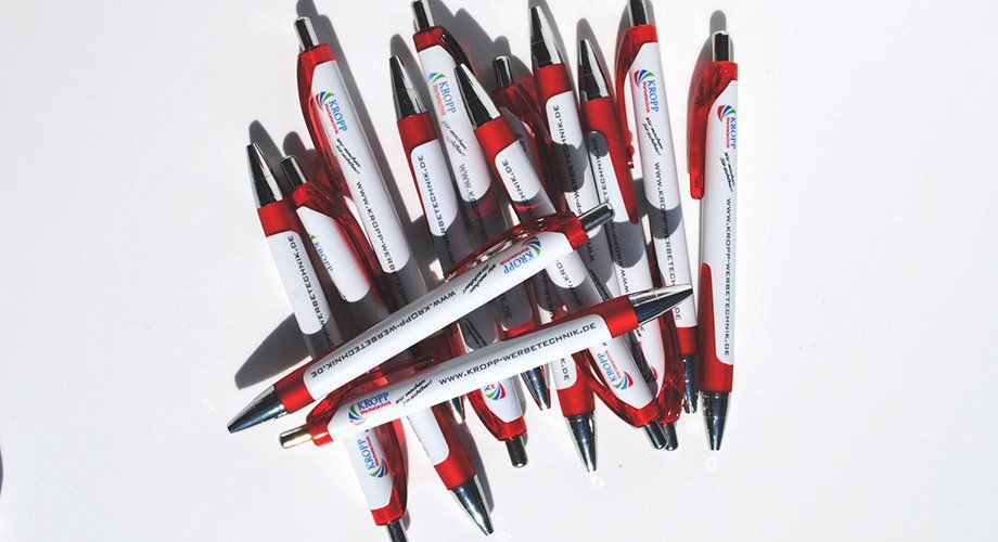 A bunch of red and white pens are stacked on top of each other on a white surface.