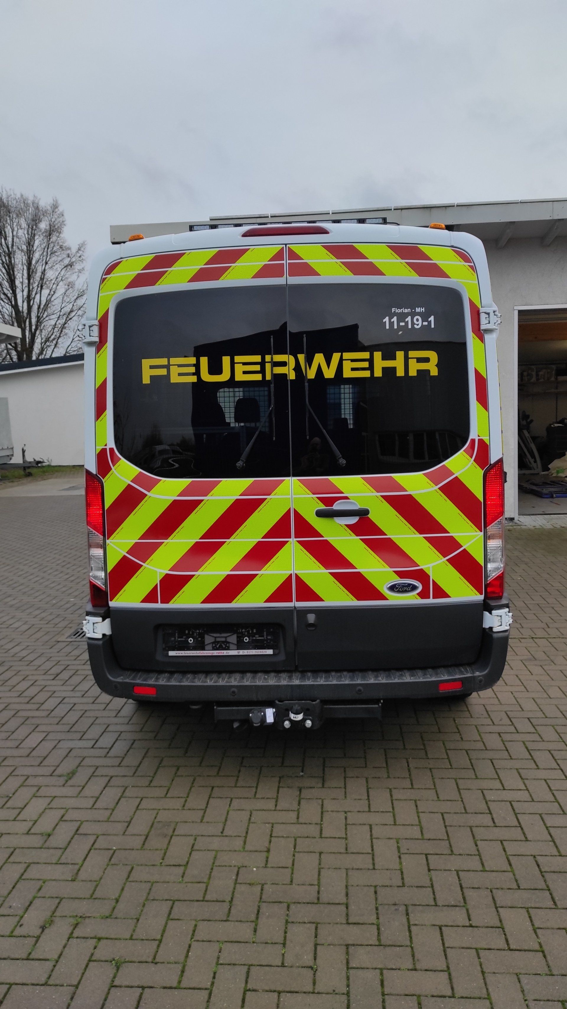 A red and yellow van with the word feuerwehr on the back is parked on a brick driveway.