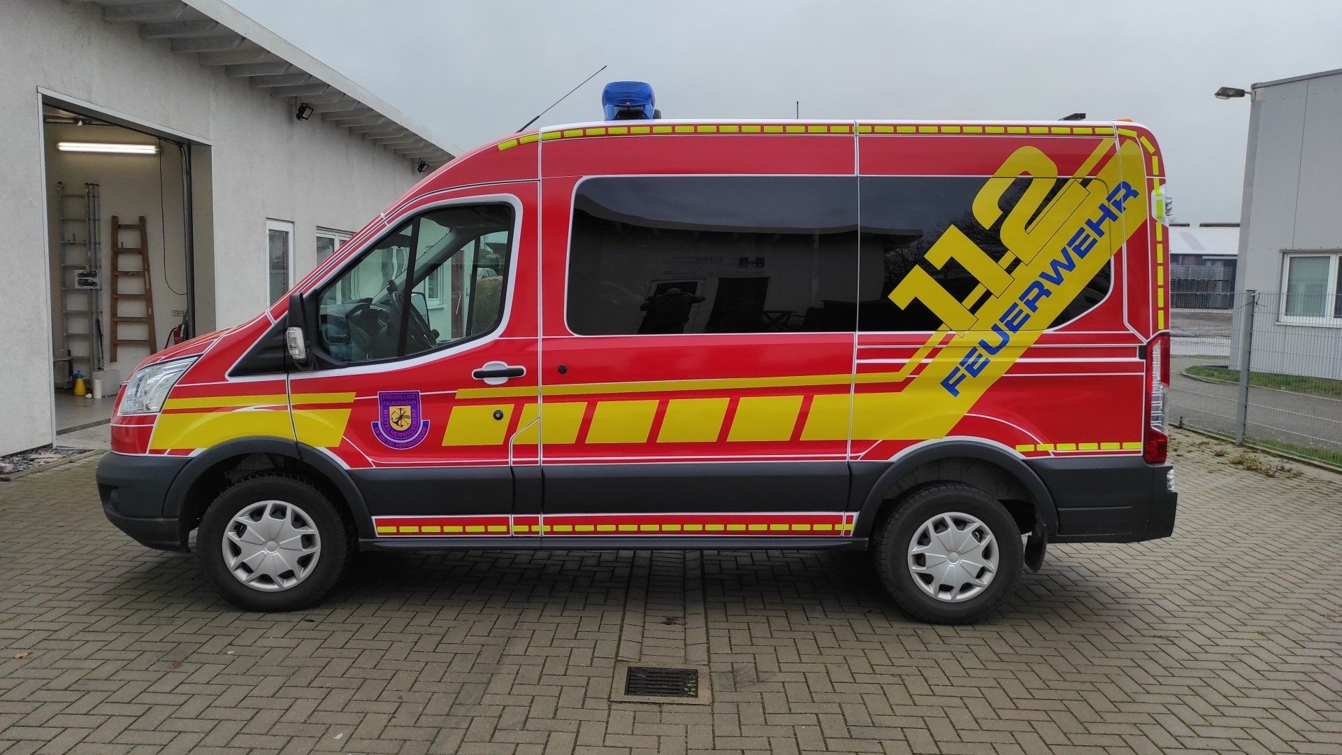 A red and yellow van with the number 112 on the side is parked in front of a building.