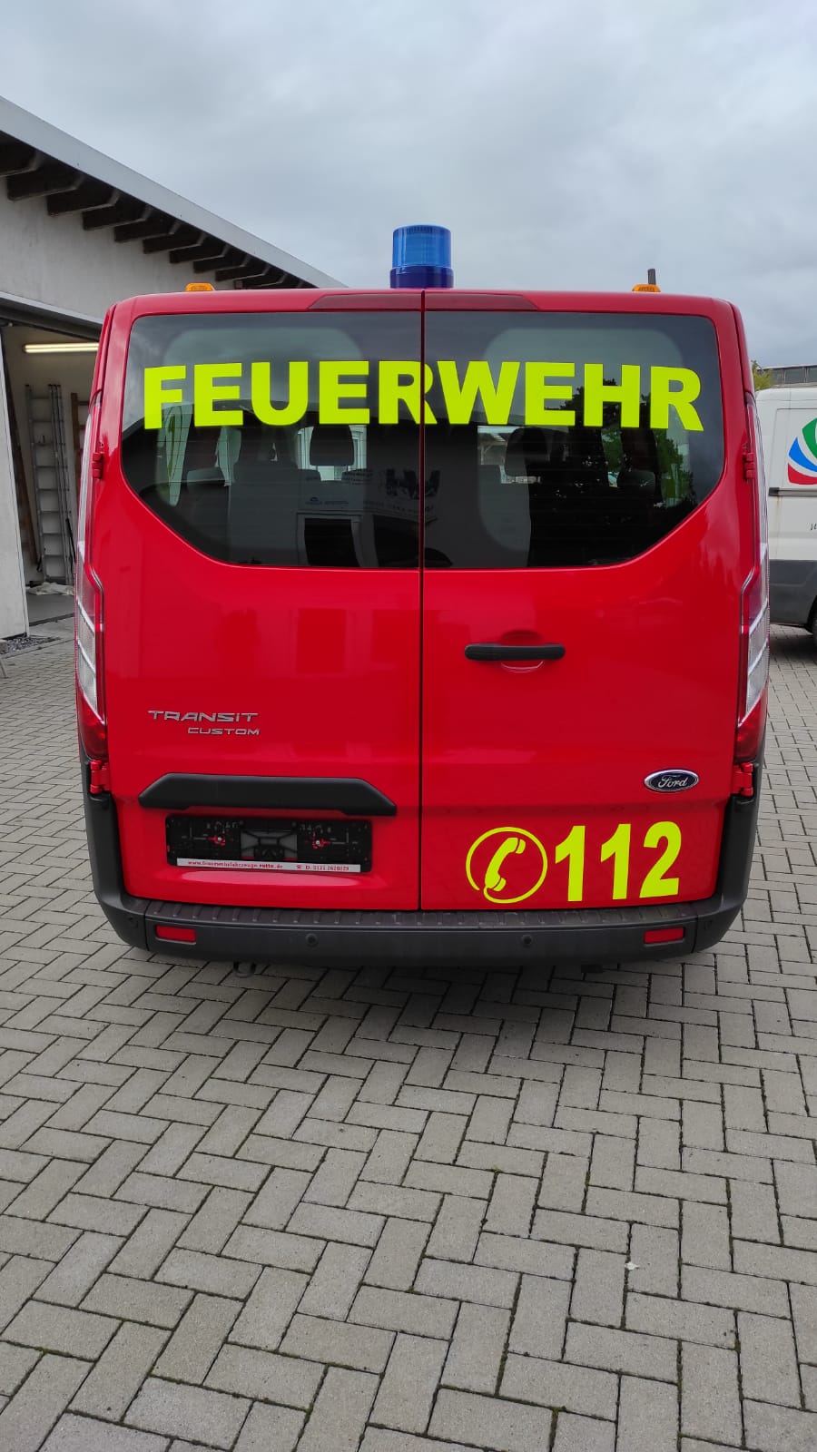 A red van with the word feuerwehr on the back is parked on a brick driveway.