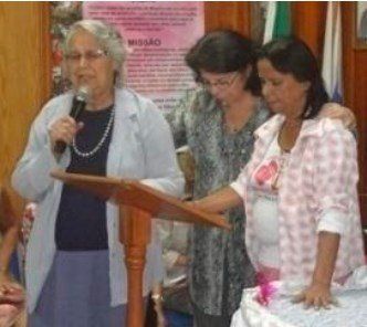 Um grupo de mulheres está de pé ao redor de um pódio com uma mulher segurando um microfone.